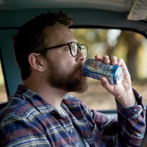 Mann mit Autoschlüssel steht neben geparktem Auto, während ein Polizist im Hintergrund näherkommt.