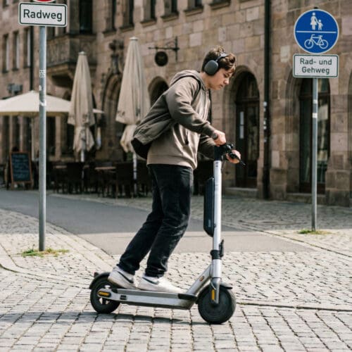 Ein Jugendlicher fährt zügig und abgelenkt mit einem E-Scooter auf einem städtischen Radweg.