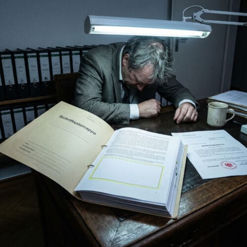 Ein gebeugter Anwalt fixiert frustriert die leere Textstelle einer formellen Begründungsschrift.