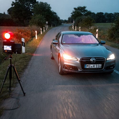 Ein greller roter Blitz einer Radarfalle reflektiert auf der Windschutzscheibe eines schnell fahrenden Autos.